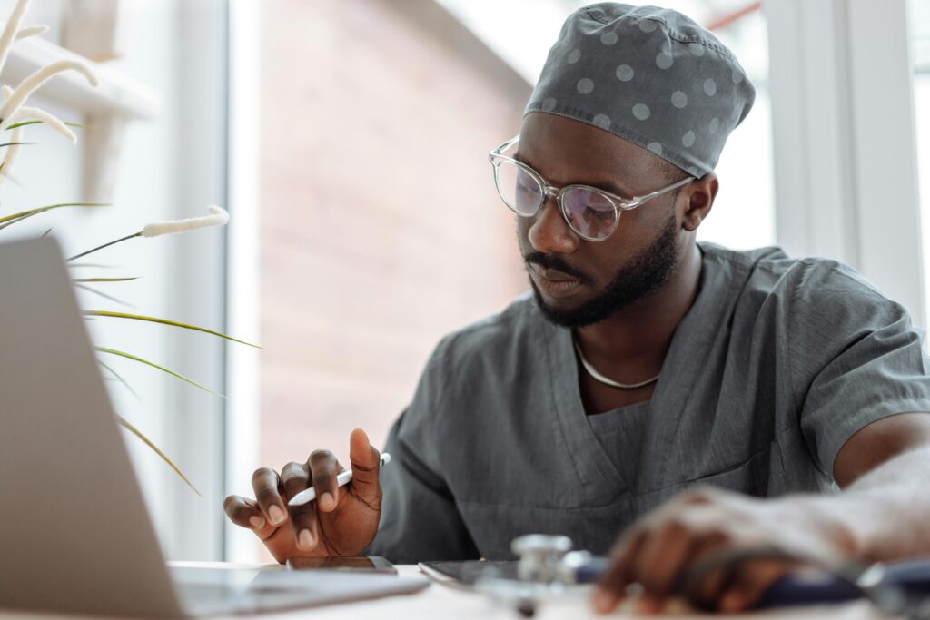 A medical practitioner seated at a table, working, with an open laptop in front of them.