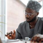 A medical practitioner seated at a table, working, with an open laptop in front of them.